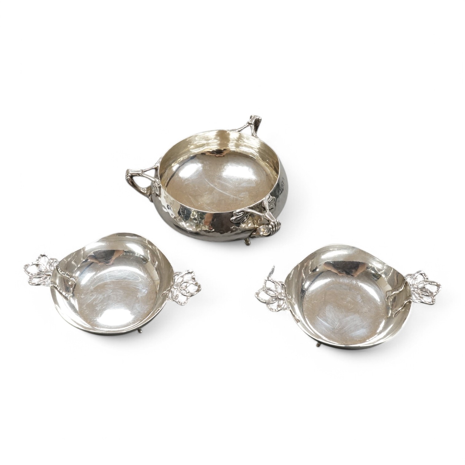 An Edwardian Art Nouveau planished silver tri-handled bowl by Charles Edwards, London, 1905, with stylised handles, diameter 94mm excluding handles, together with a pair of later silver two handled bonbon dishes, Deakin